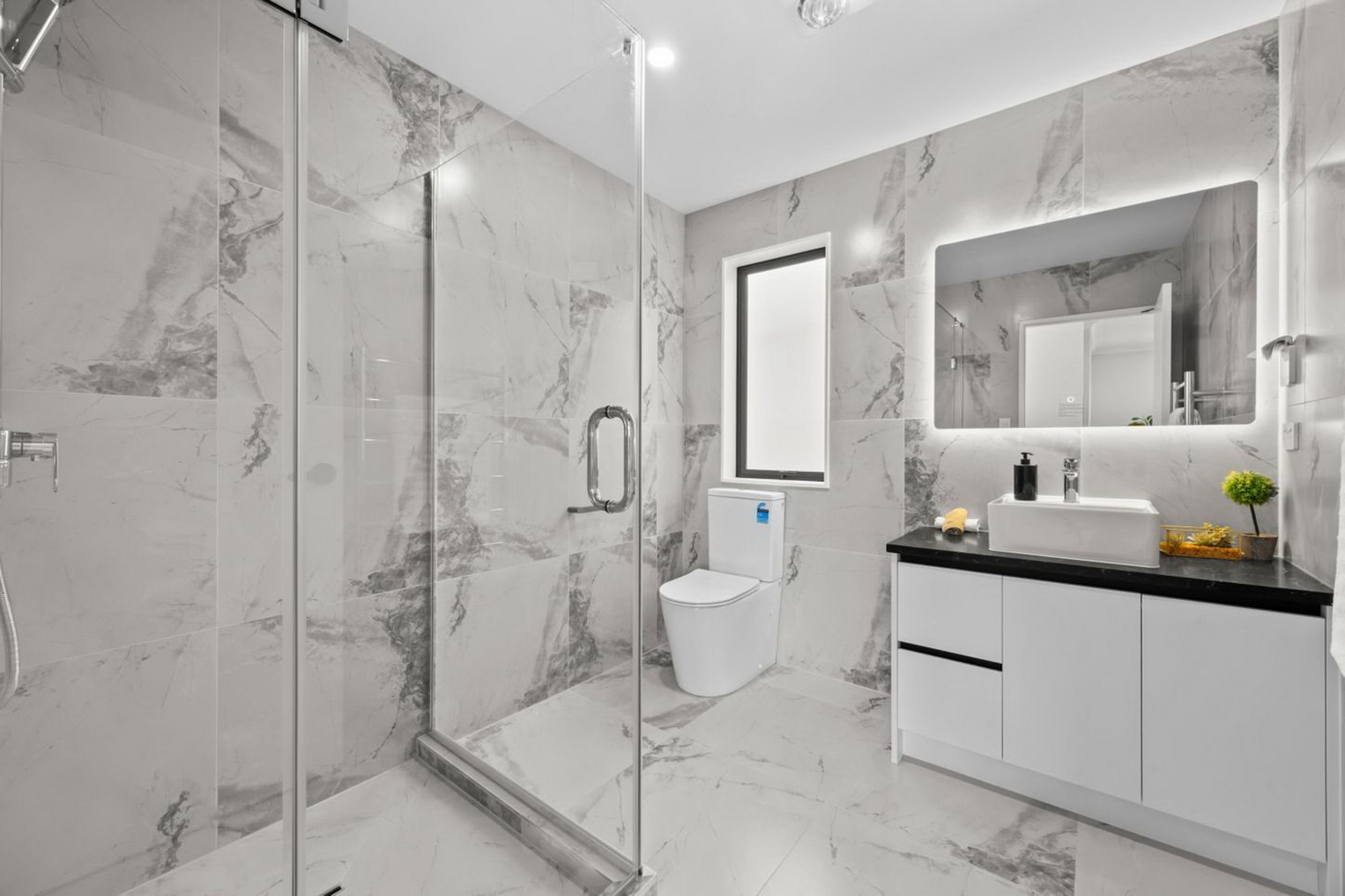 Un baño moderno con ducha de vidrio, inodoro y lavamanos con espejo.