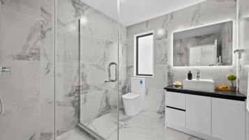 Un baño moderno con ducha de vidrio, inodoro y lavamanos con espejo.