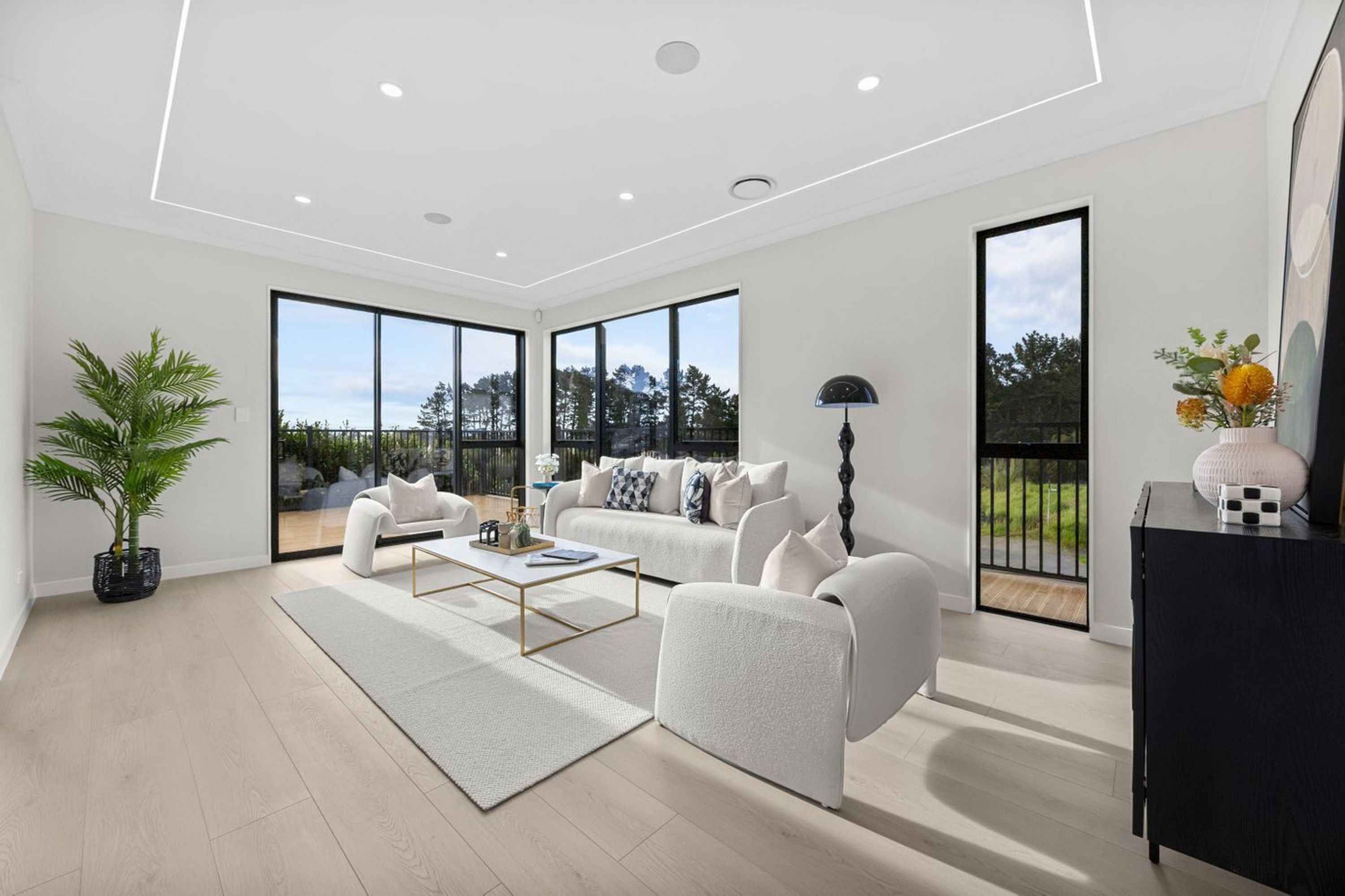 A modern living room with a white sofa set, a coffee table, and a large window offering a view of the outdoors.