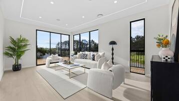 A modern living room with a white sofa set, a coffee table, and a large window offering a view of the outdoors.