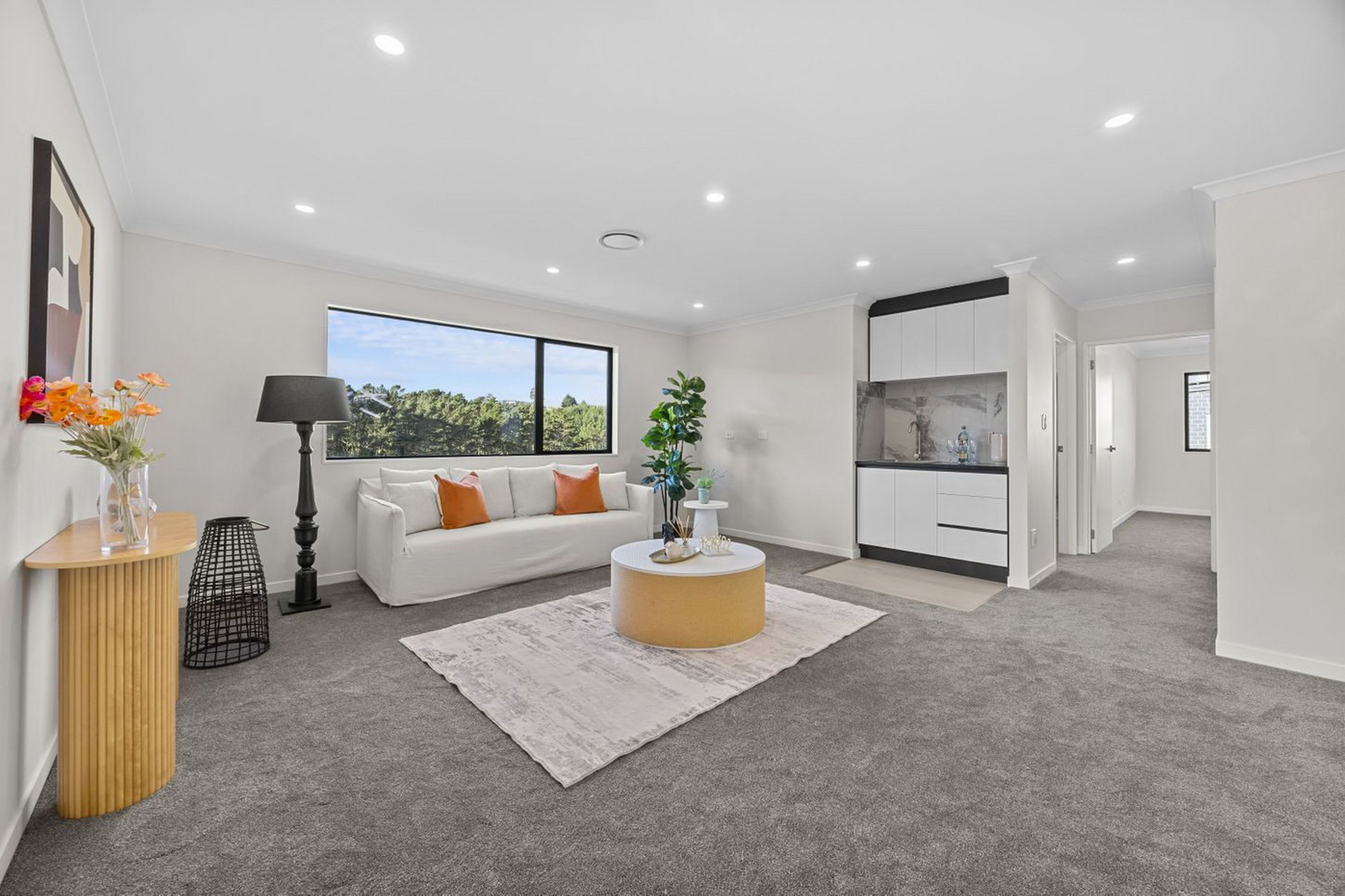A modern living room with a white sofa, a coffee table, and a view of greenery outside.
