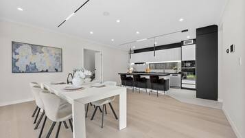 A modern kitchen with a central island, bar stools, and a dining area with a white table and chairs.