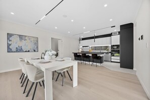 A modern kitchen with a central island, bar stools, and a dining area with a white table and chairs. - Luxury Corner New Home | Central AC | 4 Ensuites | Total 5.5 BH (Tāmaki Makaurau)