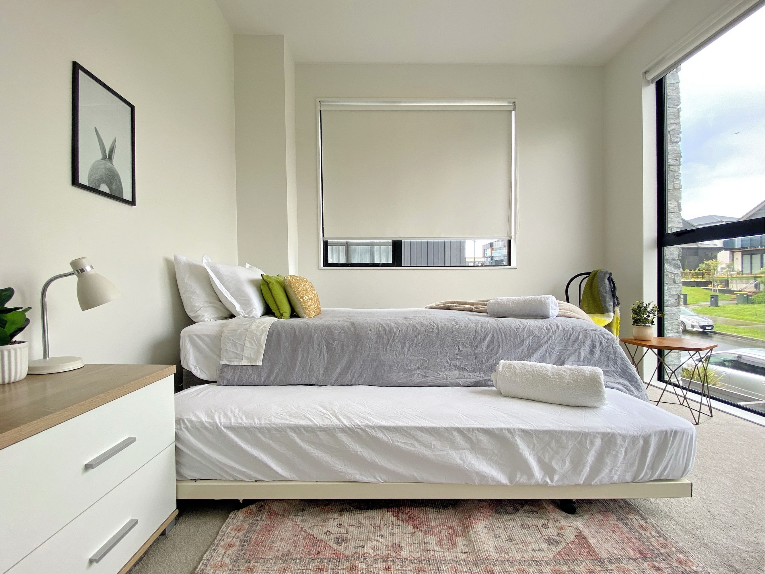 A modern bedroom with a bed, bedside table, lamp, and a view of the outdoors.