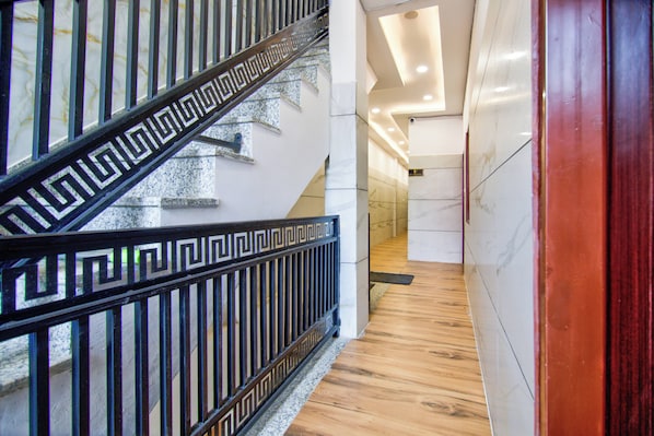 Una escalera con un diseño geométrico en la barandilla, que conduce a un pasillo con piso de mármol y un letrero que indica un área de estacionamiento.