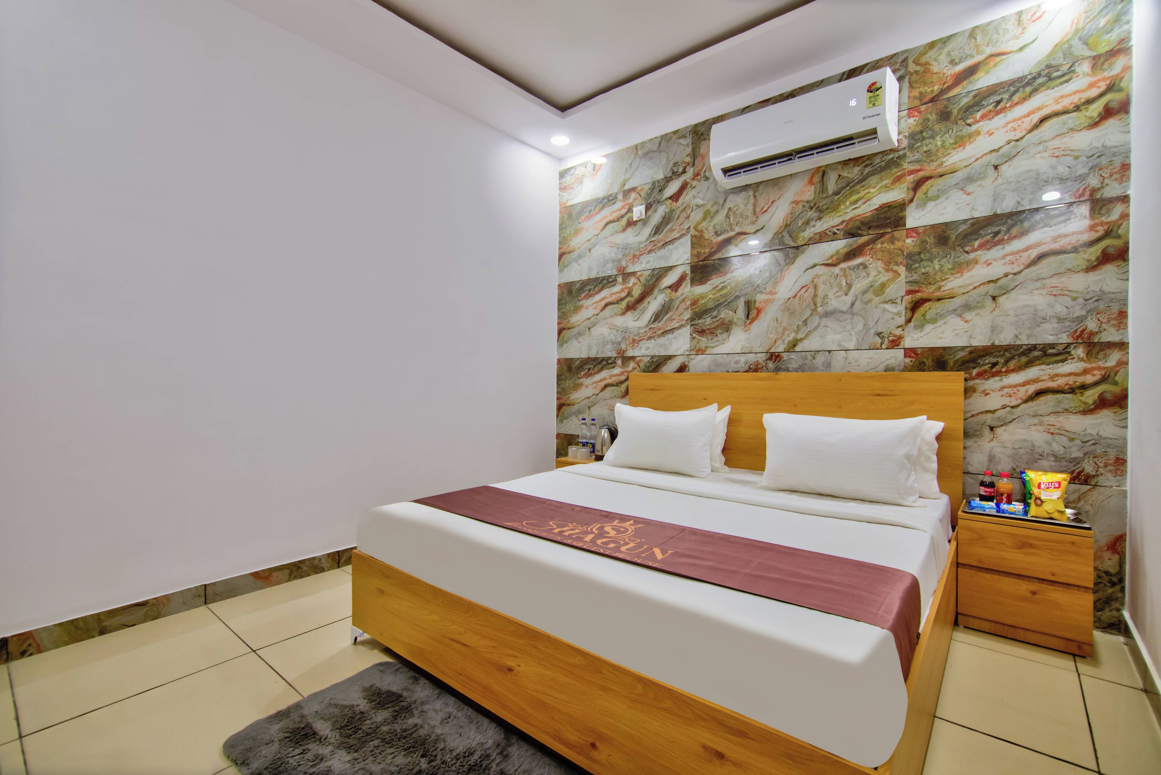 Habitación de hotel con pared de diseño de mármol, estructura de cama de madera, cubrecama blanco y una mesita de noche con aperitivos.