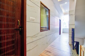 A hallway with a wooden door, a marble wall, and a window. - FabHotel Shagun (Rohtak)