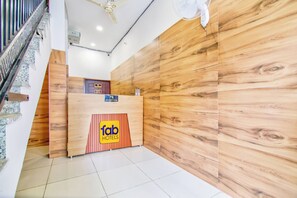 A hotel reception desk with a wooden finish, a reception area, and a staircase.