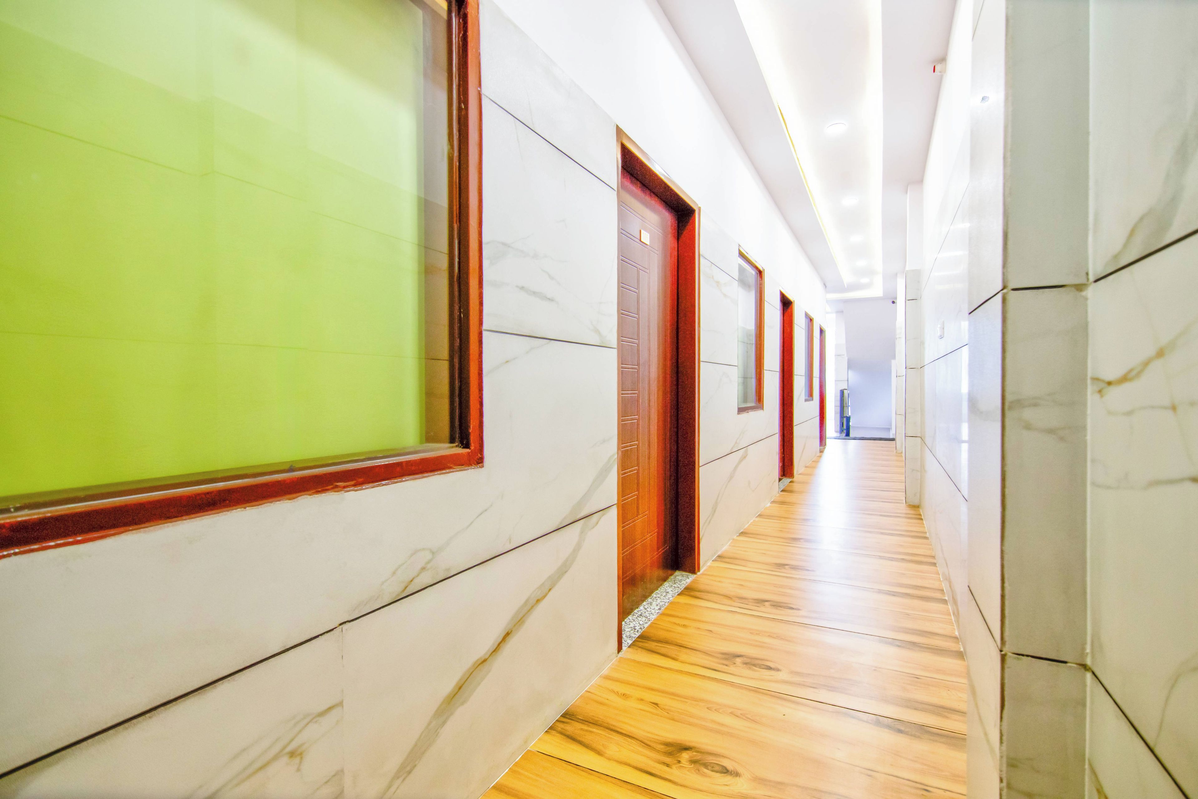 Un pasillo con paredes de mármol y piso de madera, que conduce a una puerta con marco rojo.