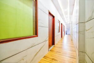 A corridor with marble walls and wooden flooring, leading to a door with a red frame.