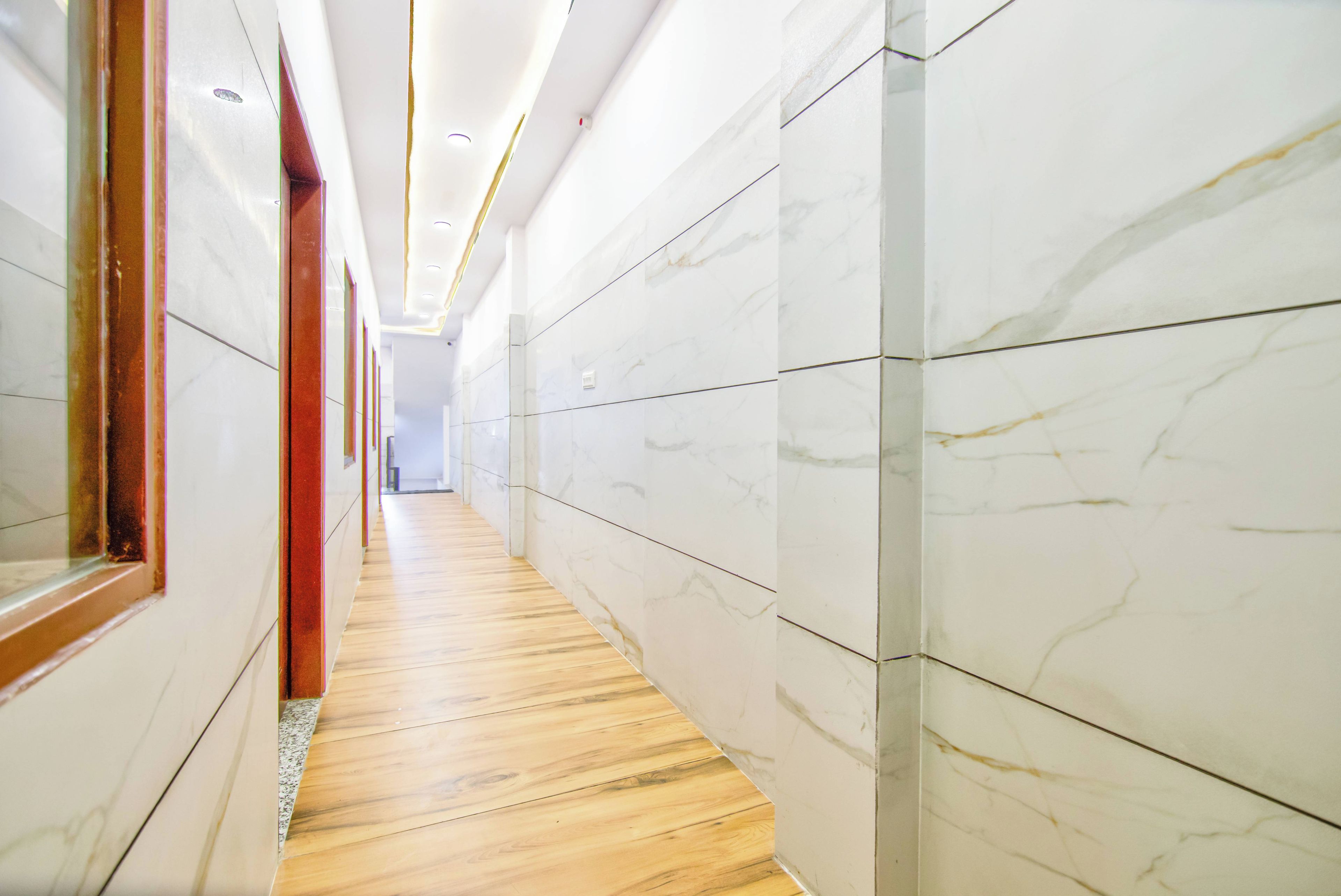 Un pasillo con paredes de mármol y suelo de madera que conduce a un espacio interior luminoso.