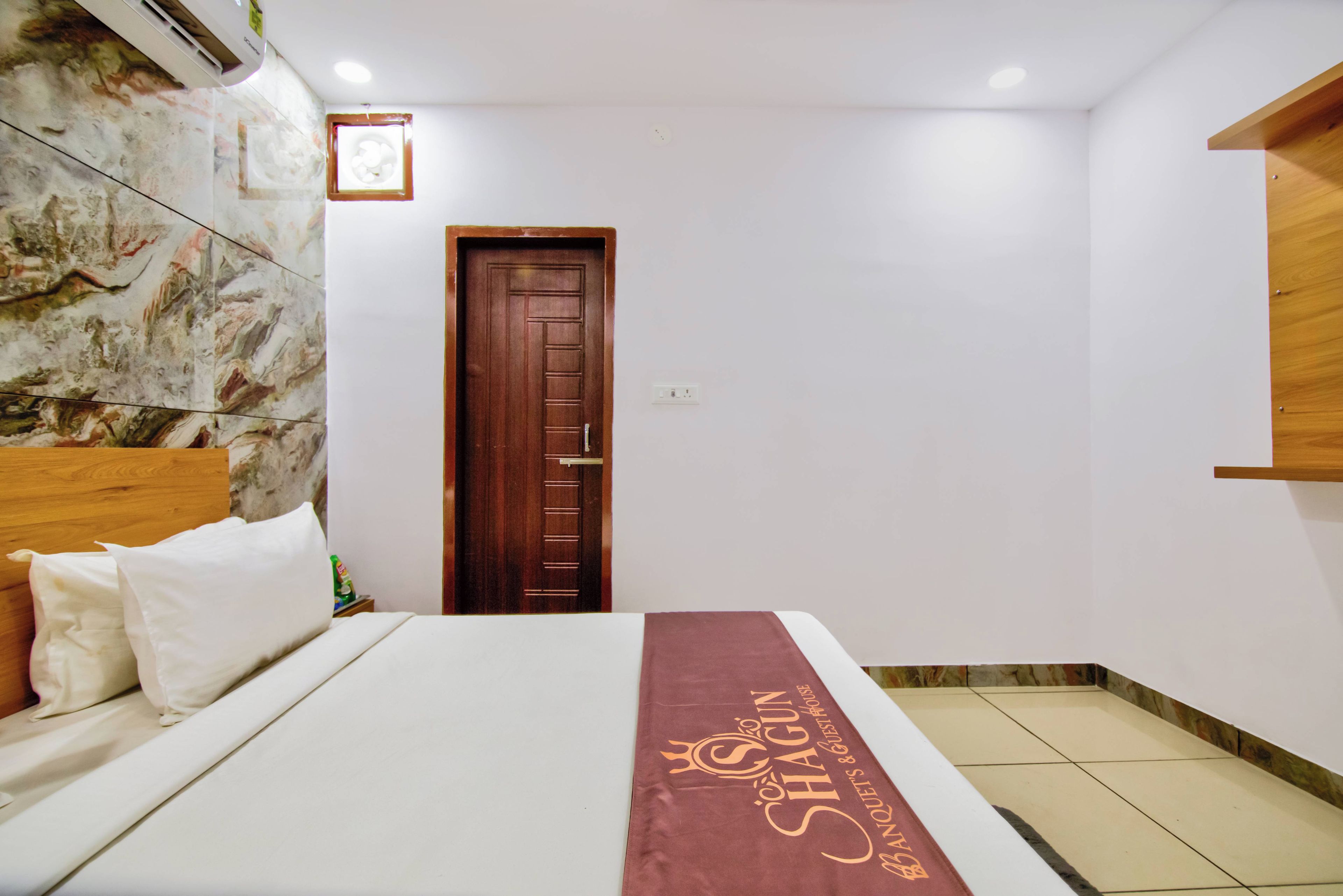 A hotel room with a bed, a wooden door, a marble wall, and a tiled floor.