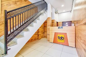 Un mostrador de recepción con un cartel que dice 'fab hotels' y una escalera con escalones de madera y barandilla de metal.