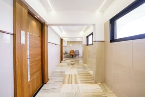 A hallway with a wooden door on the left, a tiled floor, and a window on the right. - FabHotel Host Inn (Mumbai)