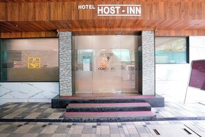 The entrance of a hotel with a wooden facade, a glass door, and a sign that reads 'HOTEL HOST - INN'. - FabHotel Host Inn (Mumbai)