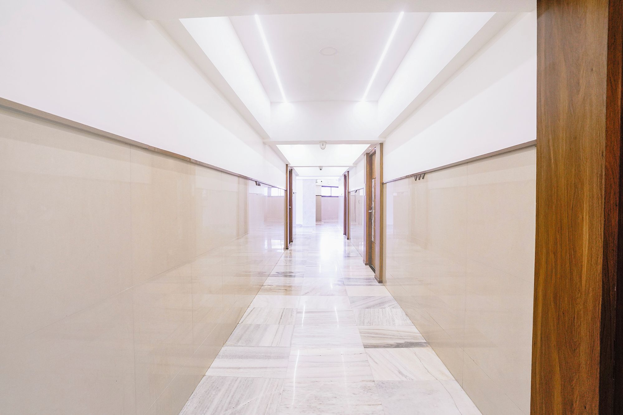 A corridor with a polished floor, doors on both sides, and a ceiling with recessed lighting.