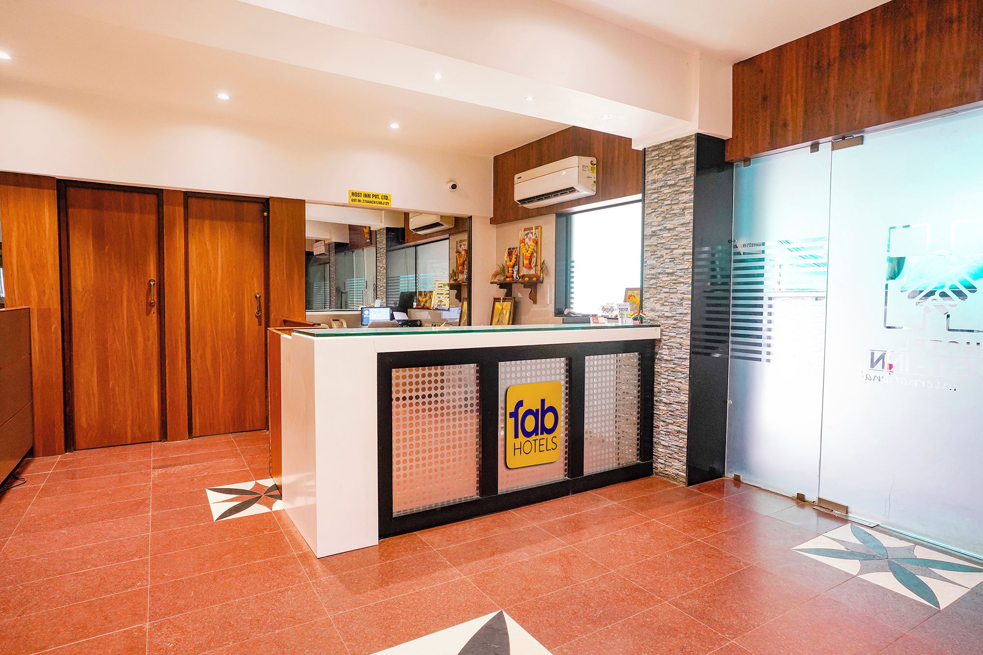Zona de recepción de hotel con un mostrador, un letrero que dice 'fab hotels' y un equipo de aire acondicionado instalado en la pared.
