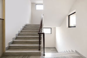 A staircase with marble steps and a metal handrail, leading to a landing with a small window. - FabHotel Host Inn (Mumbai)