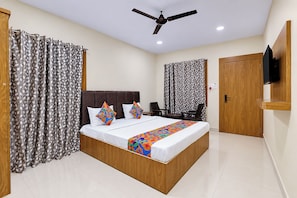 Una habitación de hotel con cama, cortinas, ventilador de techo, televisión y puerta.