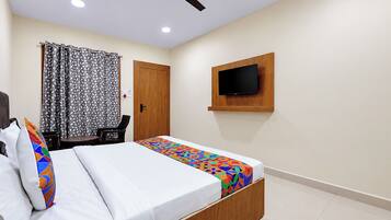 Una habitación de hotel con una cama, un televisor montado en la pared, un ventilador de techo y una ventana con cortinas.