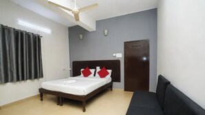 A hotel room with a bed, a ceiling fan, a wardrobe, and a dark-colored sofa. - Fabhotel Regal I (Hyderabad)