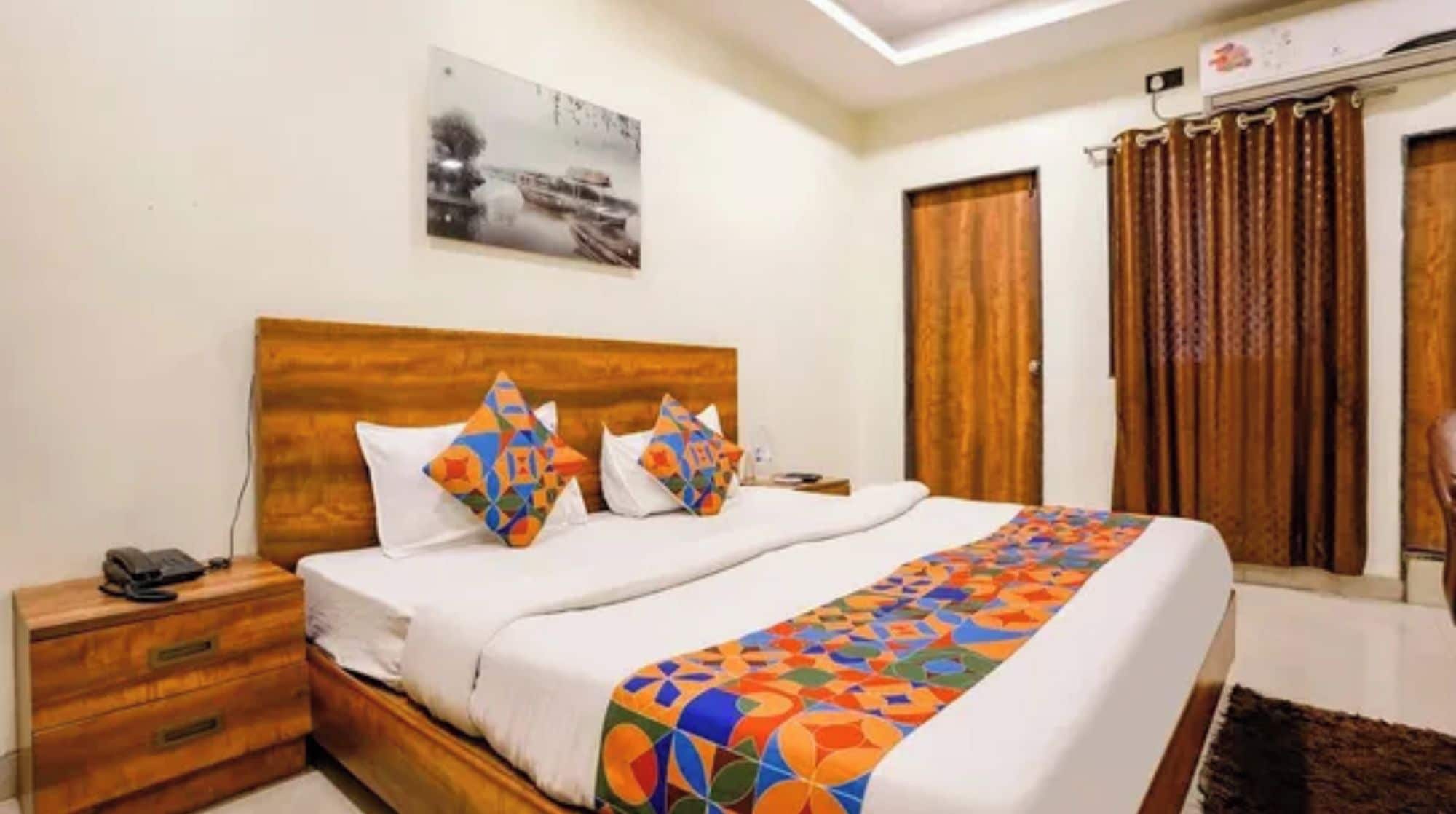 A hotel room with a wooden headboard, a bed with colorful bedding, a nightstand with a phone, and a painting on the wall.