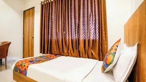A hotel room with a bed, a wooden headboard, a curtain, and a chair. - FabHotel Leo Pride (Chhatrapati Sambhajinagar)