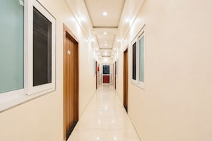 A corridor with doors on both sides, a tiled floor, and a ceiling with recessed lighting. - FabHotel Hkd Divine Stay (Vrindavan)