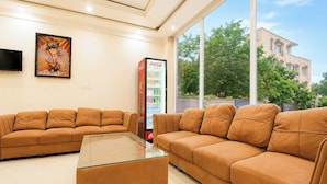 Um hall de hotel com dois sofás, uma mesa de centro de vidro, um refrigerador Coca-Cola e uma grande janela com vista para o exterior.