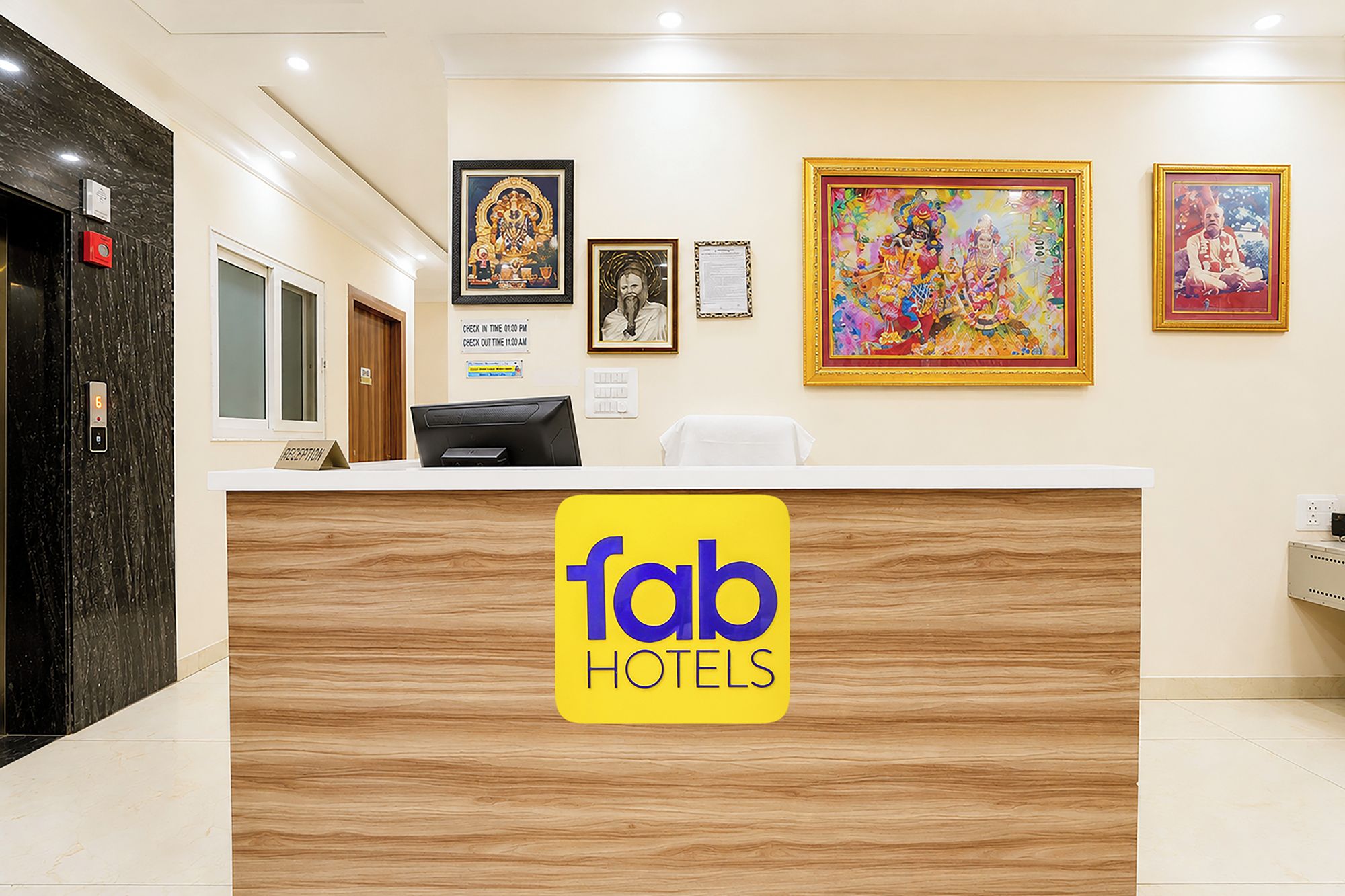 A hotel reception desk with a wooden finish, a check-in/out sign, and framed artwork on the wall.