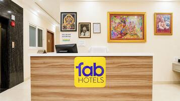 A hotel reception desk with a wooden finish, a check-in/out sign, and framed artwork on the wall.