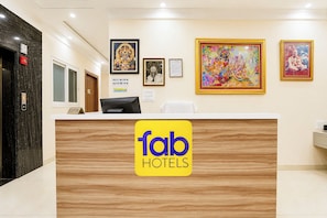 Un mostrador de recepción de hotel con detalles de madera, un cartel de registro de entrada/salida y cuadros en la pared.