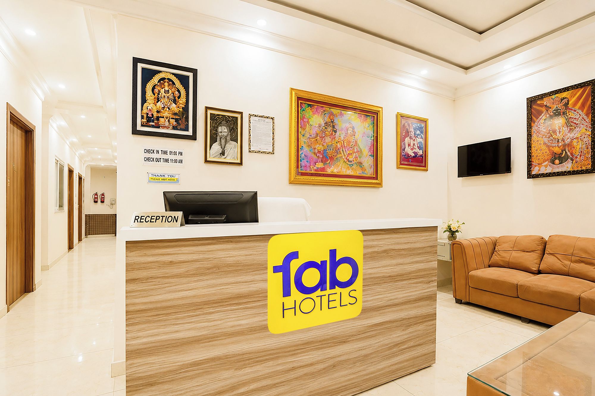 A hotel reception area with a reception desk, framed artwork, a sofa, and a television.