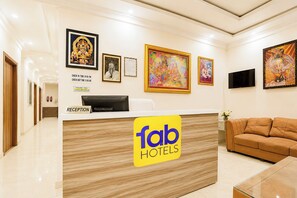 Zona de recepción de hotel con mostrador, obras de arte enmarcadas, un sofá y un televisor.