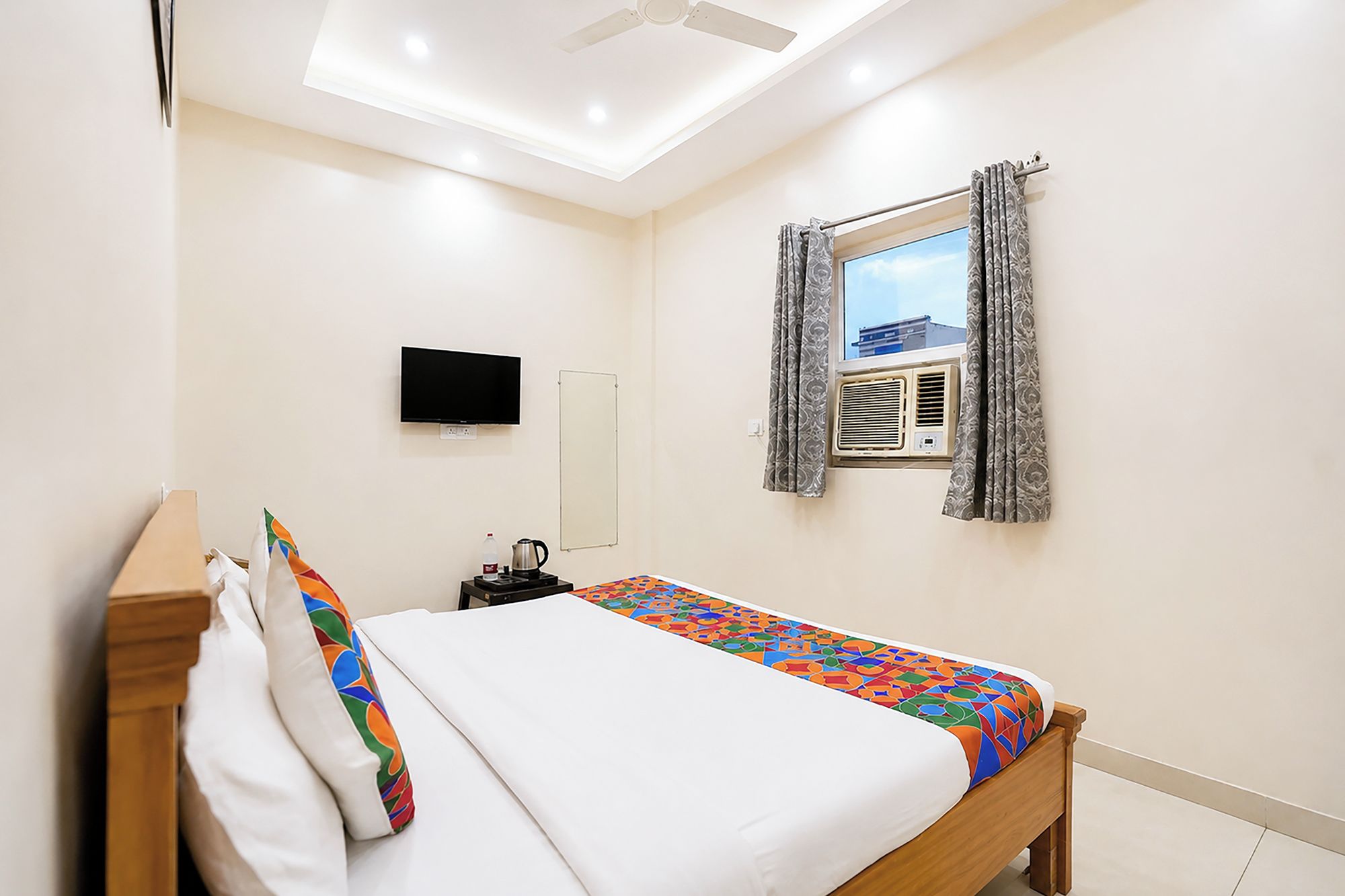 A bedroom with a bed, a flat-screen TV, an air conditioning unit, and a window with curtains.