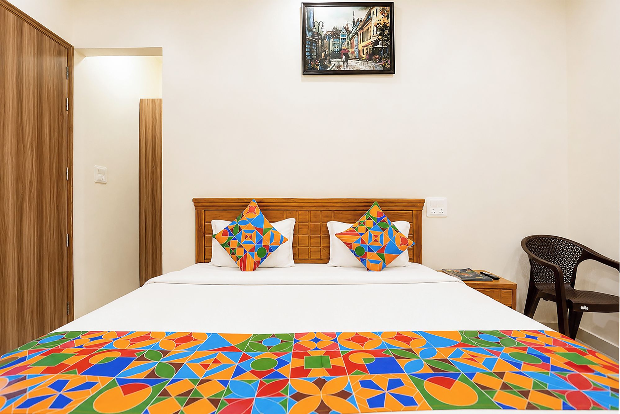 A bedroom with a bed, two pillows, a nightstand, a chair, and a painting on the wall.
