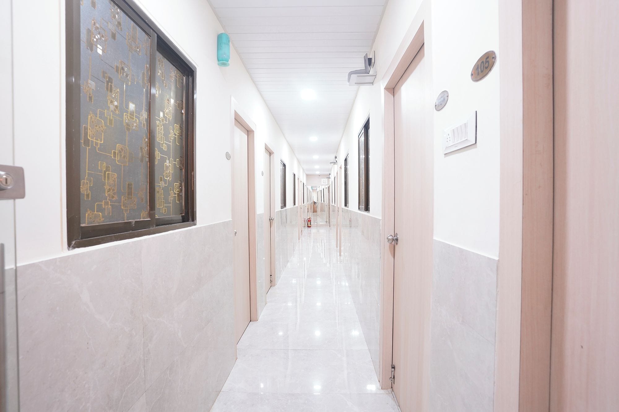 A corridor with doors on both sides, a tiled floor, and a ceiling with recessed lighting.