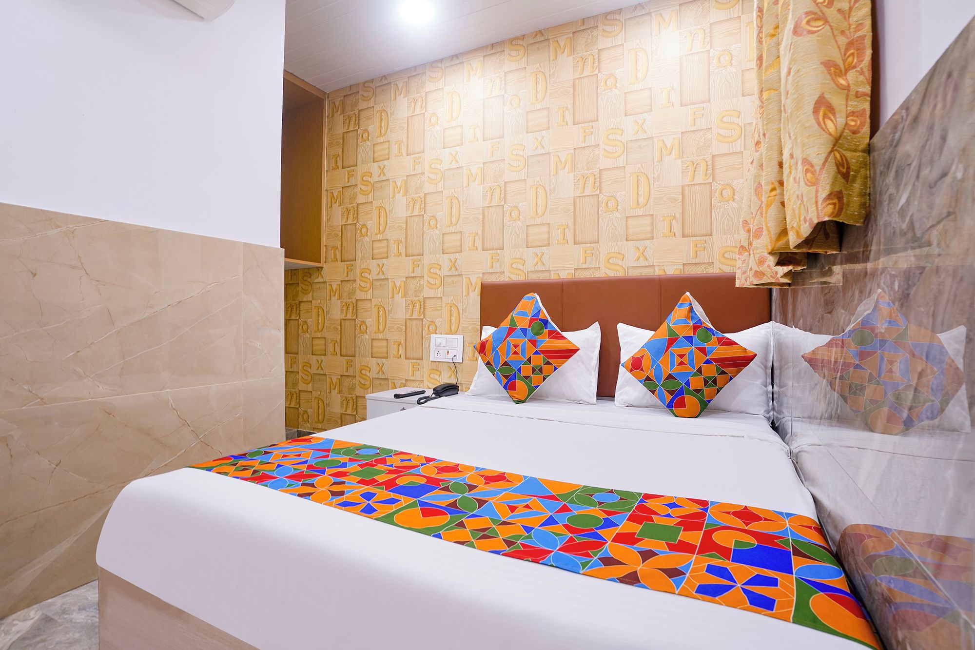 Una habitación de hotel con una cama, una pared de madera con diseños alfabéticos y una colcha estampada.