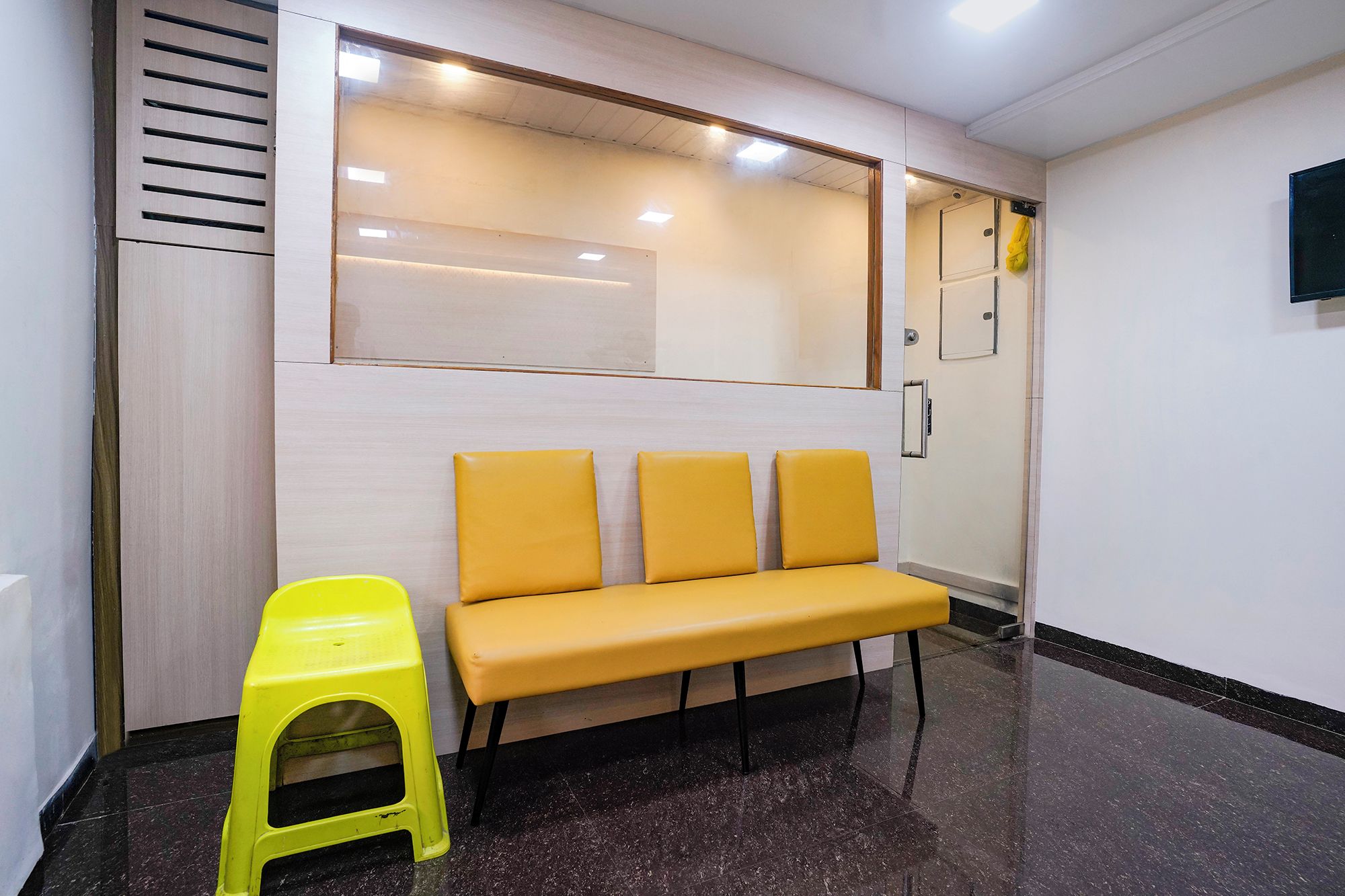 Un área de espera con un banco y un taburete amarillo.