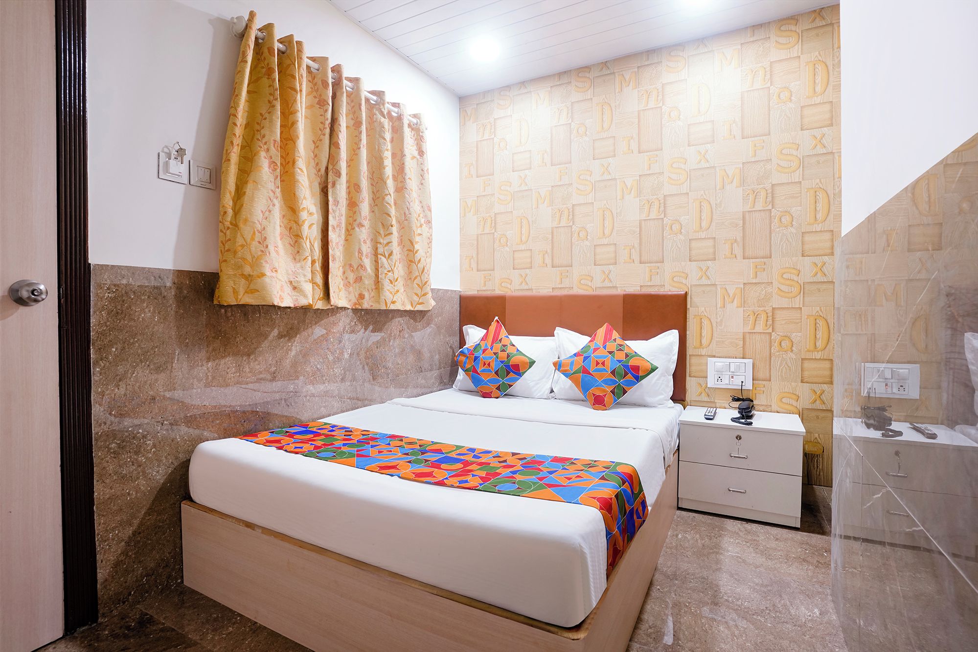 A bedroom with a bed, a nightstand, a mirror, and a wall with alphabet letters.