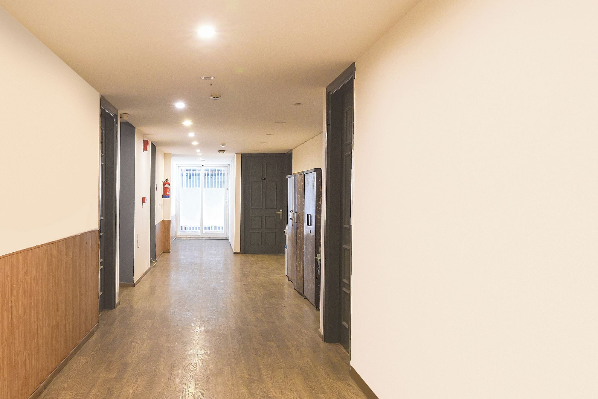 A hallway with wooden paneling on the walls, a fire extinguisher mounted on the wall, and a door at the end.