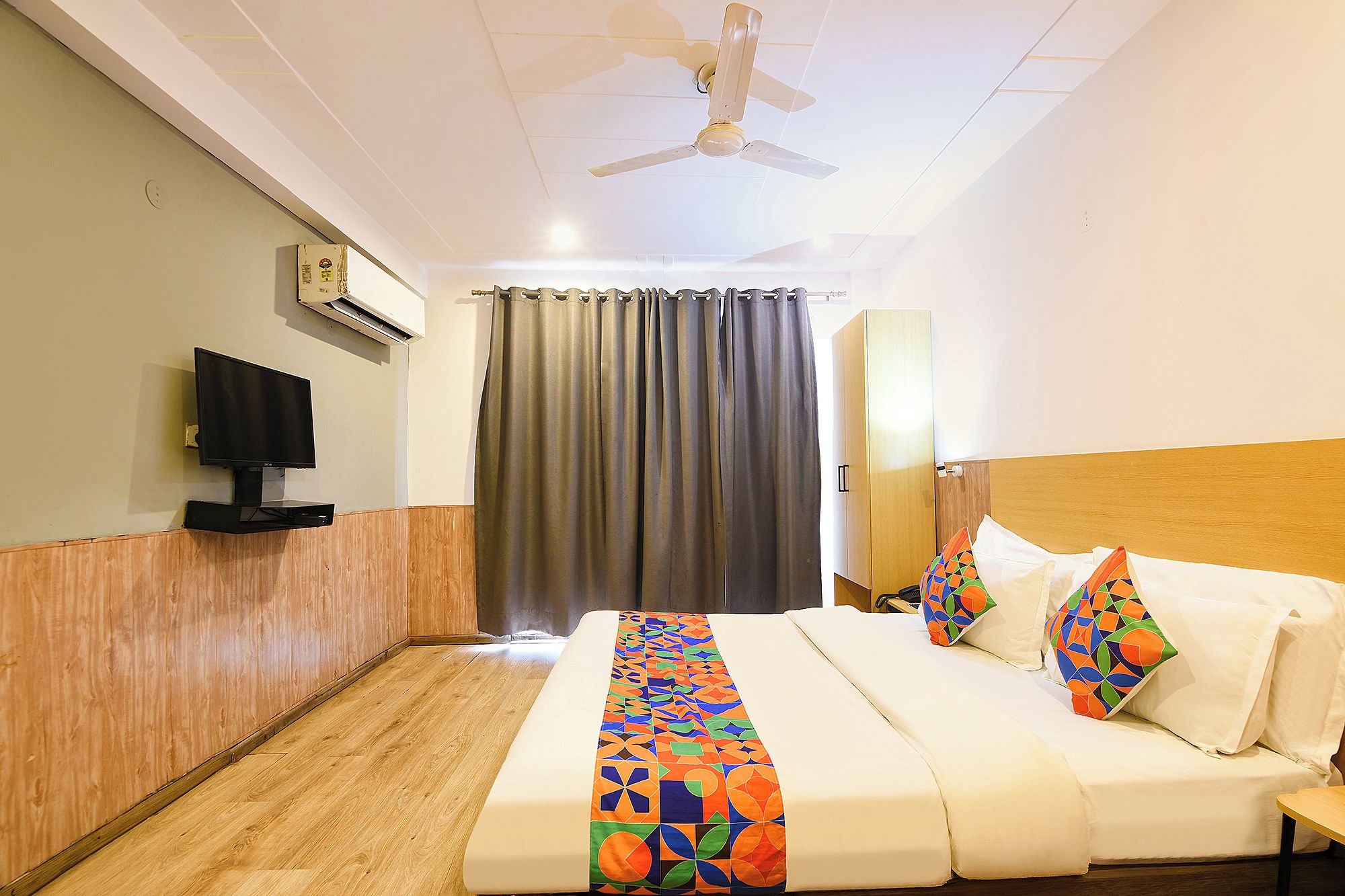 A hotel room with a bed, a television, a ceiling fan, and a window with curtains.