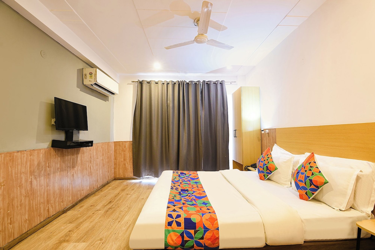 A hotel room with a bed, a television, a ceiling fan, and a window with curtains.