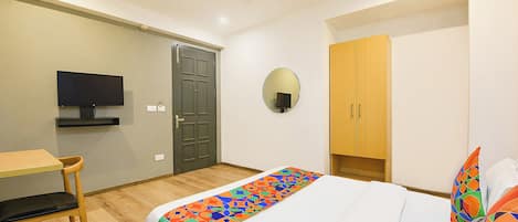 Habitación de hotel con cama, escritorio, televisor, armario y ventilador de techo.