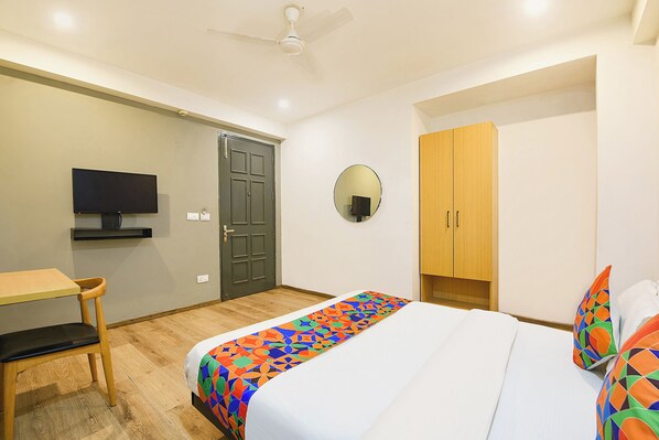 A hotel room with a bed, a desk, a television, a wardrobe, and a ceiling fan.