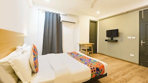 A hotel room with a bed, a desk, a chair, a television, and a door. - Fabhotel Golden Moment (Gurugram)
