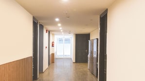 A hallway with wooden paneling on the walls, a fire extinguisher mounted on the wall, and a door at the end. - Fabhotel Golden Moment (Gurugram)