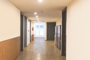 A hallway with wooden paneling on the walls, a fire extinguisher mounted on the wall, and a door at the end. - Fabhotel Golden Moment (Gurugram)