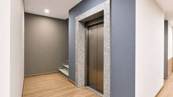 A hallway with a wooden floor, a grey wall, and a door with a textured frame.