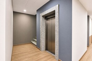 A hallway with a wooden floor, a grey wall, and a door with a textured frame.